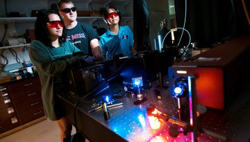 students and professor in lab wearing red protective goggles